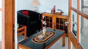 Una habitación con un armario de madera, un sofá negro, una mesita con un tapete decorativo y una lámpara colgante.