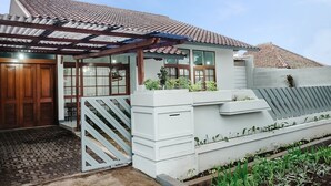 Una casa con techo de tejas, puerta de madera, porche cubierto y un jardín con plantas.