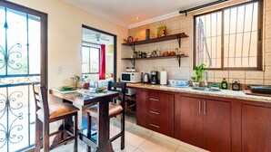 A kitchen with wooden cabinets, a countertop with various appliances, and a dining area with chairs.