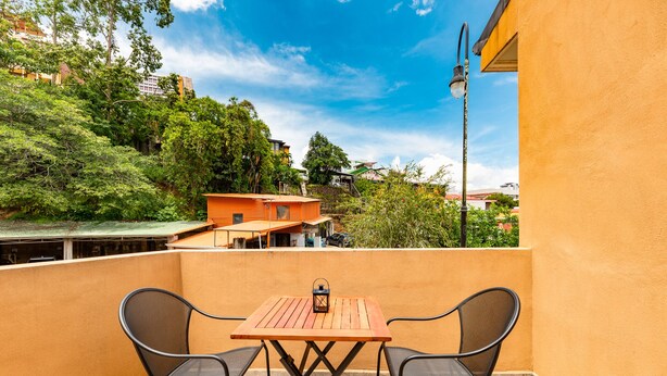 A balcony with a wooden table and two chairs, overlooking a residential area with trees and buildings.