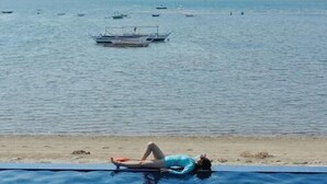 A pool with a person lying on a float, boats on the water, and a beach in the background. - El Pueblo De Hermano by Cocotel (Lian)