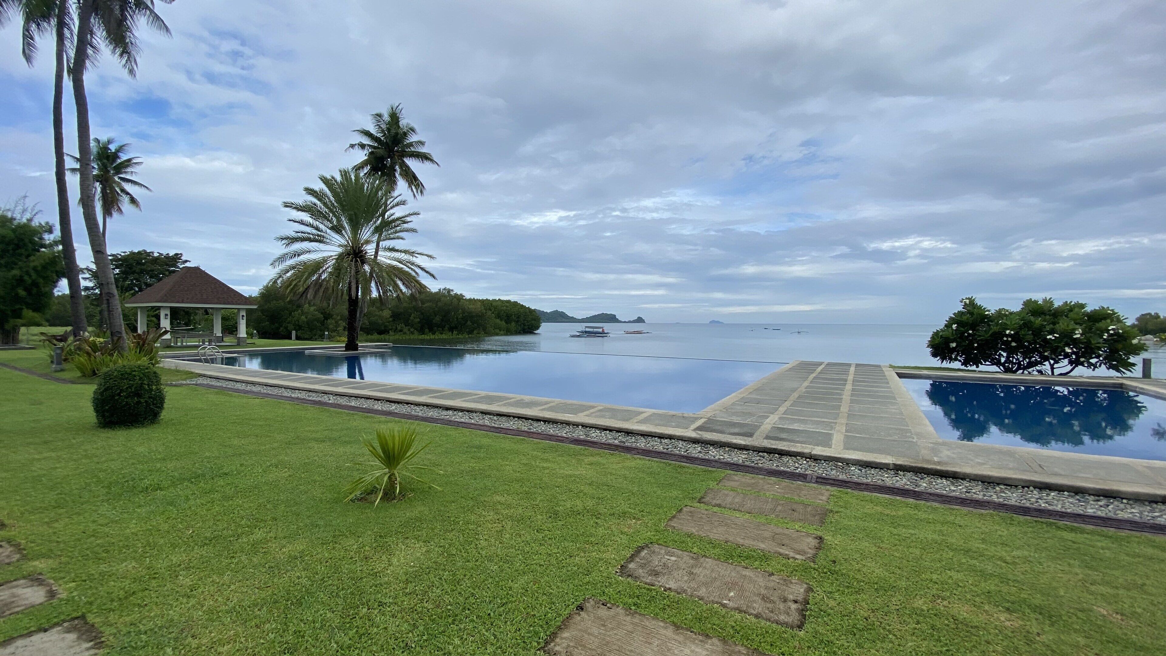 A serene pool area with a clear view of the sea, surrounded by lush greenery and a gazebo.