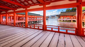 Une terrasse en bois, avec des piliers rouges, d’où l’on peut admirer les bâtiments traditionnels situés de l’autre côté de l’eau.