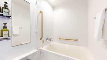 Une salle de bain moderne avec une baignoire, une douche et un miroir. On y trouve des articles de toilette sur une étagère.