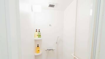 A small, white bathroom with a shower, a toilet, and a shelf with toiletries.