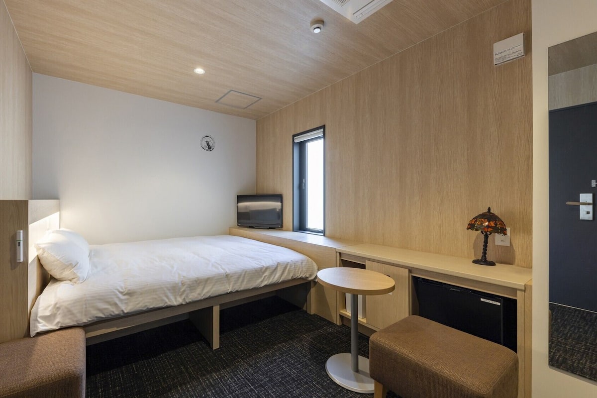 Une chambre d’hôtel comprenant un lit, un bureau, une chaise, une petite table, une lampe, un téléviseur et une armoire.