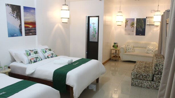 Une chambre d’hôtel avec deux lits, un canapé et une petite table. Les lampes sont fixées au mur et la porte est dotée d’un panneau en verre dépoli.