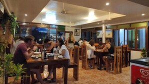 Un restaurant avec des tables et des chaises en bois, des plantes d’intérieur et une vue sur la ville la nuit.