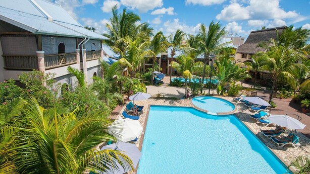 Un resort con una piscina grande, palmeras y un edificio con techo de paja.