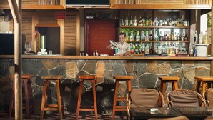 Una zona de bar con taburetes de madera, una pared de piedra y estantes llenos de botellas.