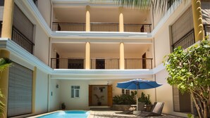 Un edificio de varios pisos con piscina, mobiliario exterior y una palmera.
