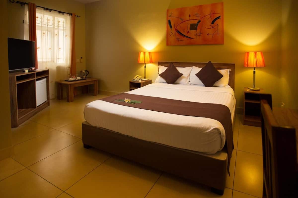 Quarto de hotel com uma cama grande, duas luminárias de cabeceira, uma TV de tela plana, uma escrivaninha e uma cafeteira.