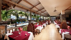 Restaurante con terraza al aire libre, techado de metal y mesas dispuestas con manteles blancos y servilletas rojas.