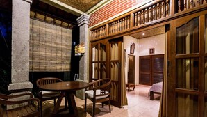 A traditional room with a wooden table and chairs, a bed, and a brick wall. - Bali Asli Lodge by EPS (Ubud)