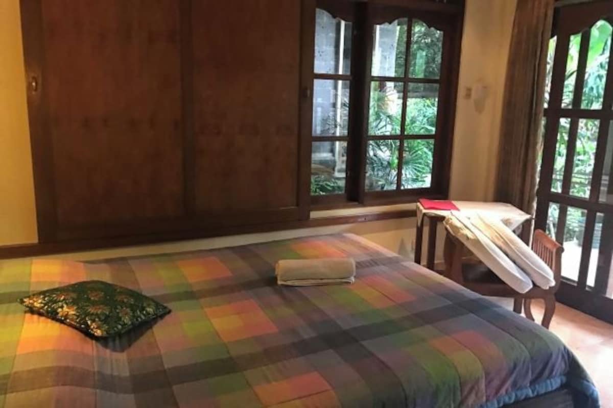Een kamer met een bed, een raam en een tafel waarop een rood object ligt.