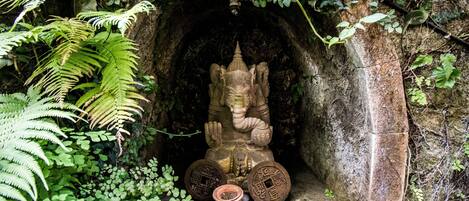 Une statue de pierre représentant une divinité, placée dans une niche et entourée de fougères et de feuillage.