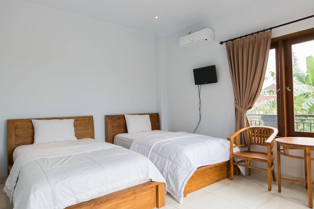 A bedroom with two wooden beds, a television mounted on the wall, a window with curtains, and a wooden chair and table.