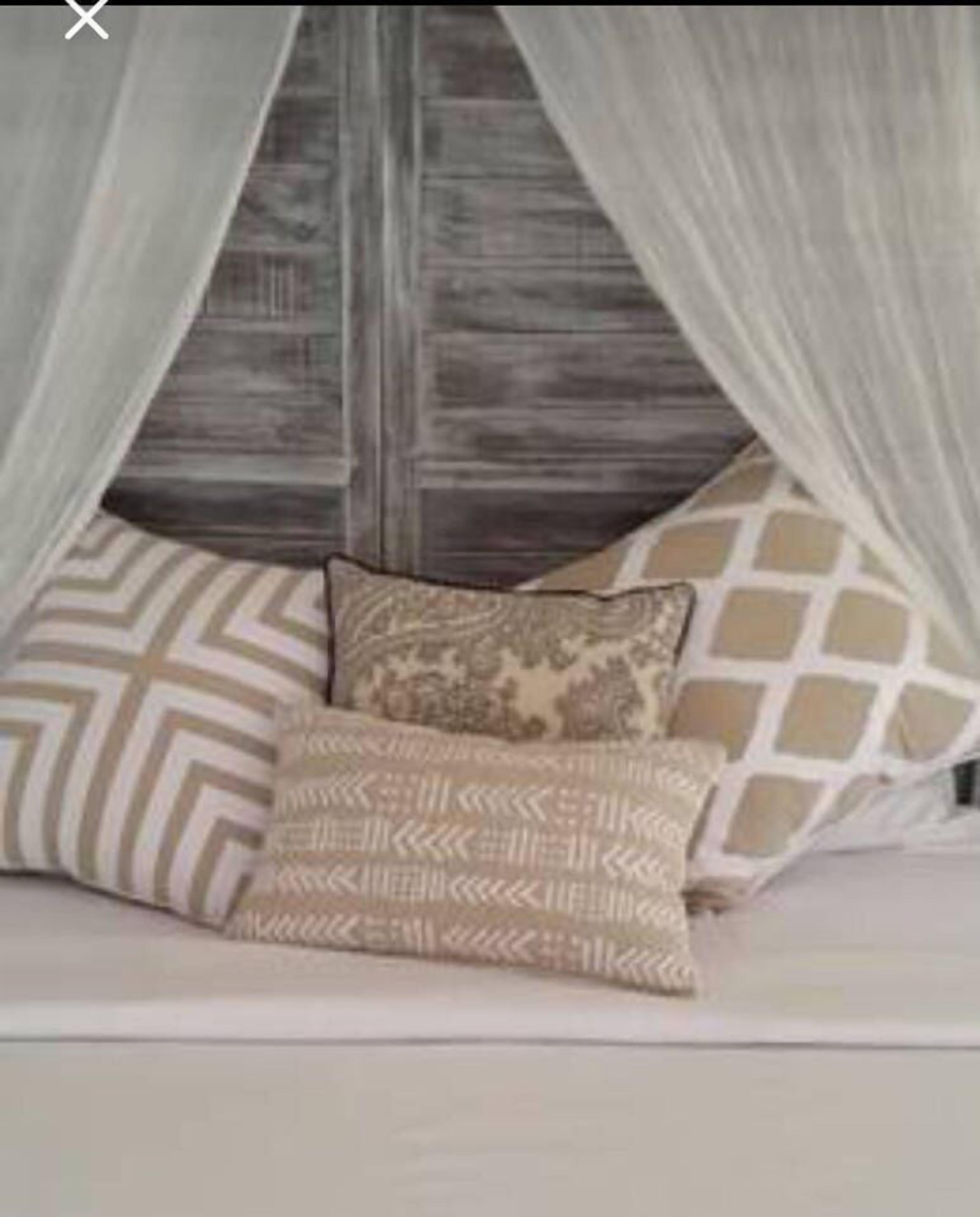 Un lit à baldaquin, avec des coussins à motifs et une tête de lit en bois.