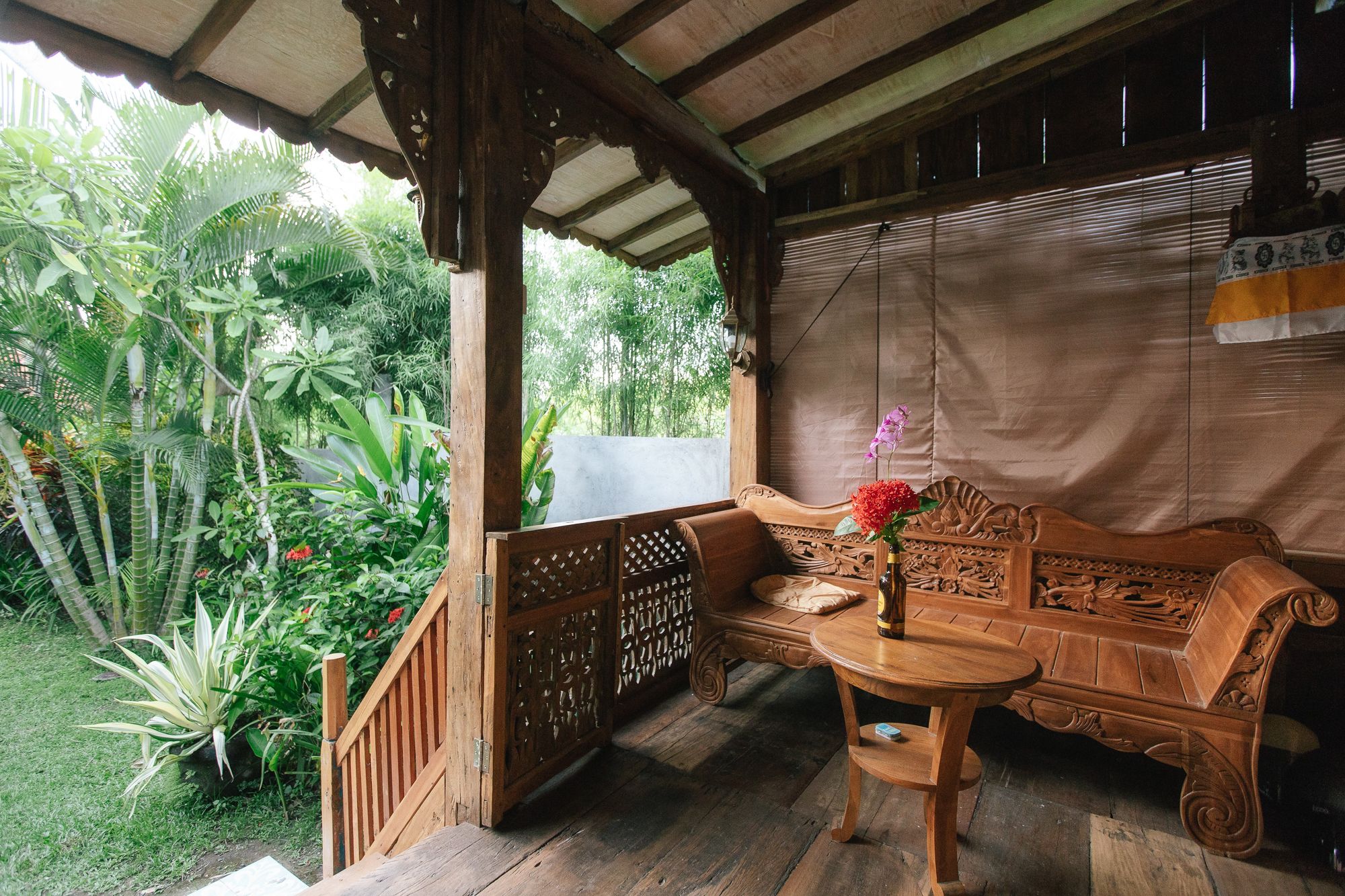 A wooden bench with intricate carvings, a small table with a vase of flowers, and a view of lush greenery outside.