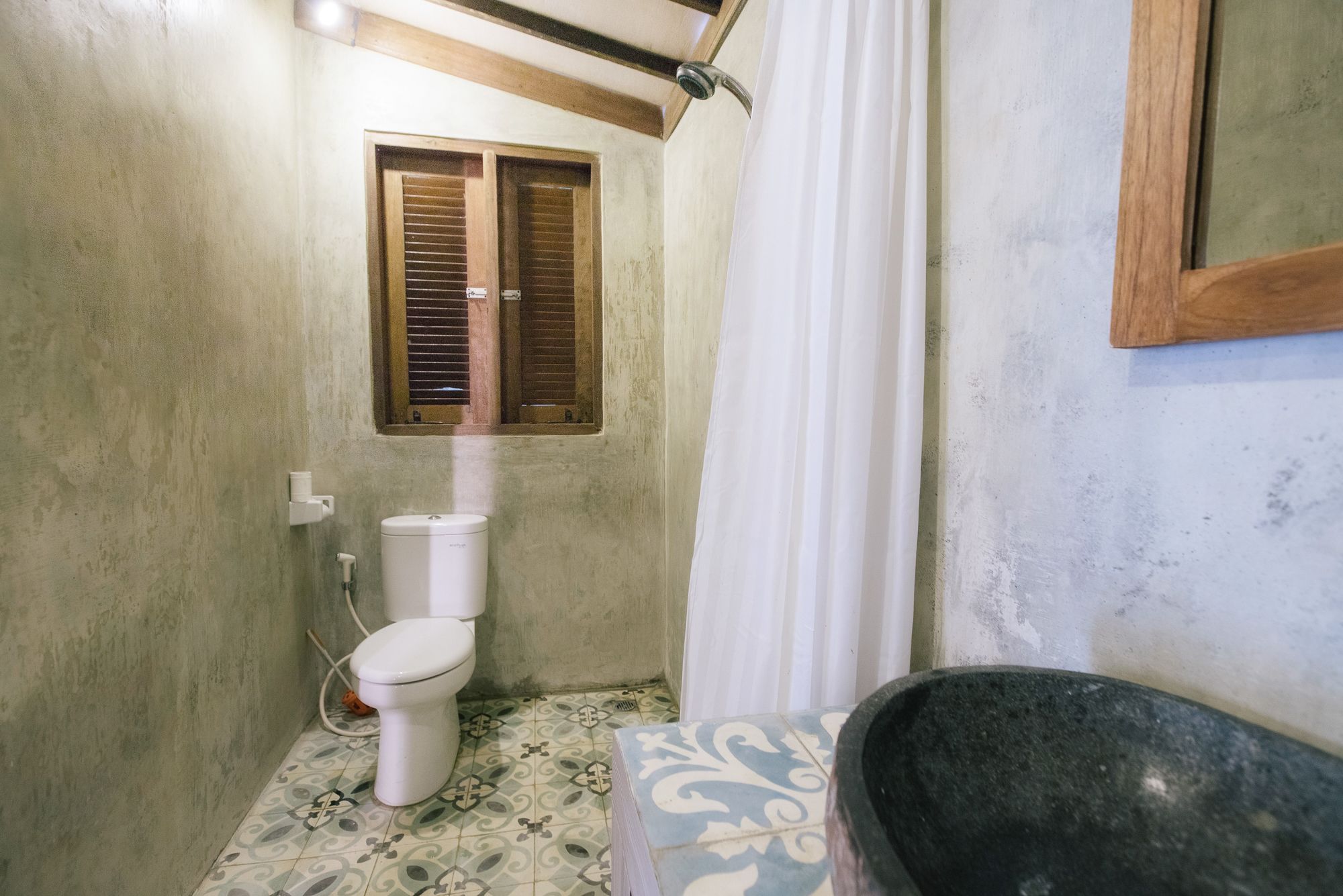A bathroom with a toilet, a window with wooden shutters, a shower curtain, and a bathtub.