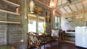 A rustic kitchen with wooden shelves, a dining area with two chairs, and a refrigerator. - Pande Homestay (Canggu)