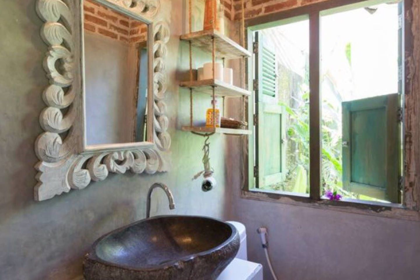 Un baño con un lavabo grande y rústico, un espejo con ornamentales tallas y una ventana con vistas a la vegetación.