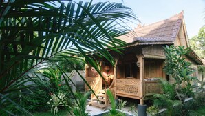 A traditional wooden house with a porch, surrounded by lush greenery and a well-maintained garden. - Pande Homestay (Canggu)