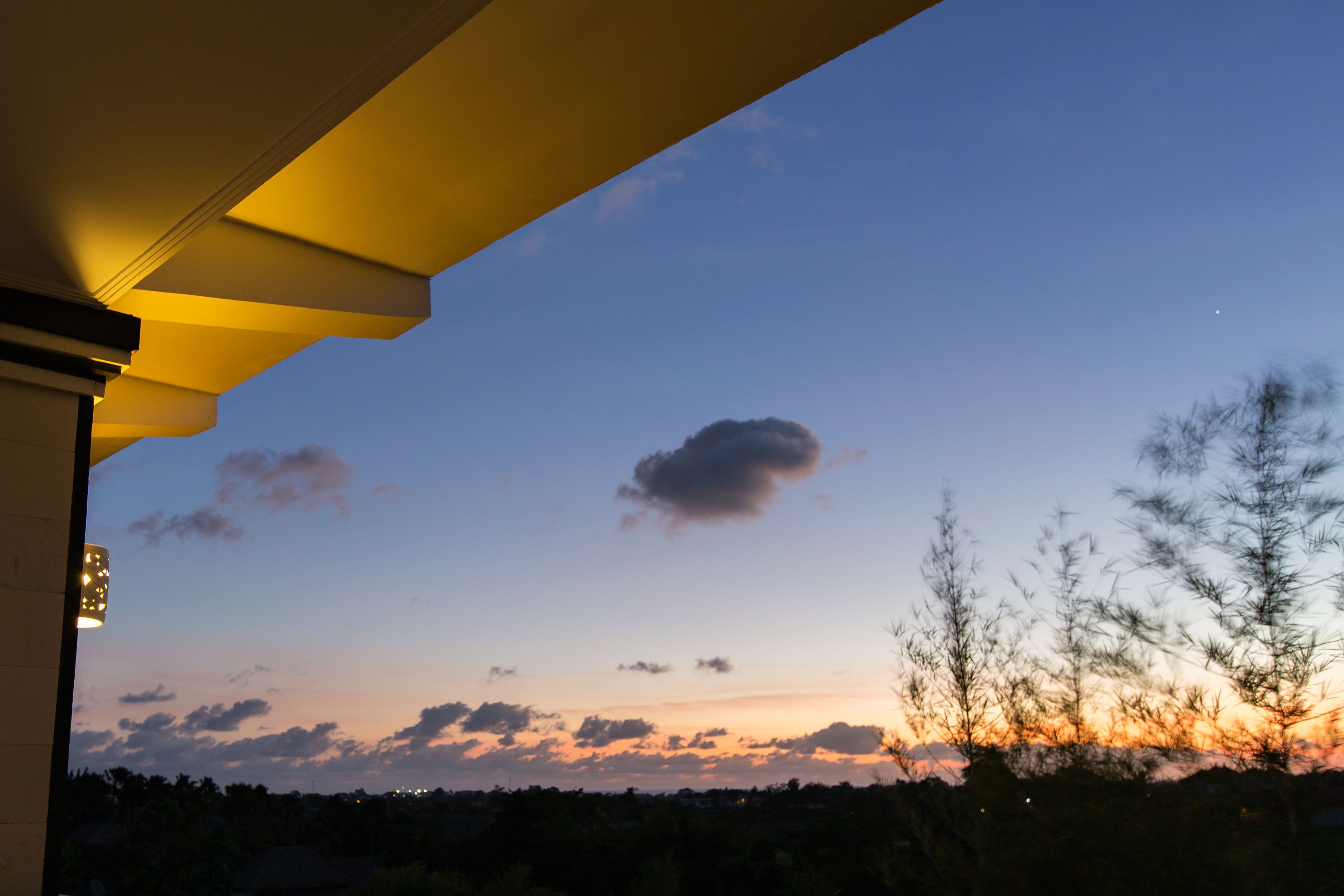 A sunset view from a covered outdoor area with a clear sky and distant trees.