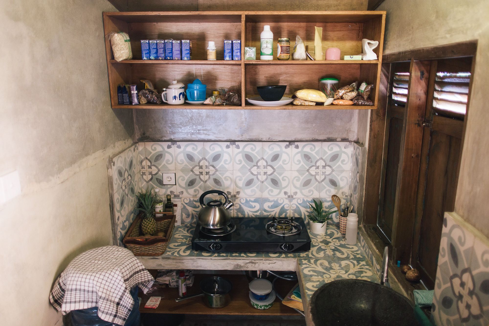 A compact kitchen with a gas stove, shelves with food items, and a patterned backsplash.