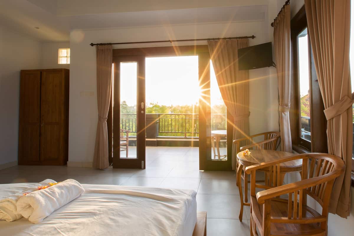 A hotel room with a bed, wooden furniture, a balcony with a table and chairs, and a TV mounted on the wall.
