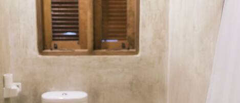 A small bathroom with a toilet, a window with wooden shutters, and a shower area.
