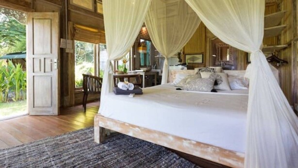 A bedroom with a four-poster bed, a desk with a chair, and a view of the outdoors. - Pande Homestay (Canggu)