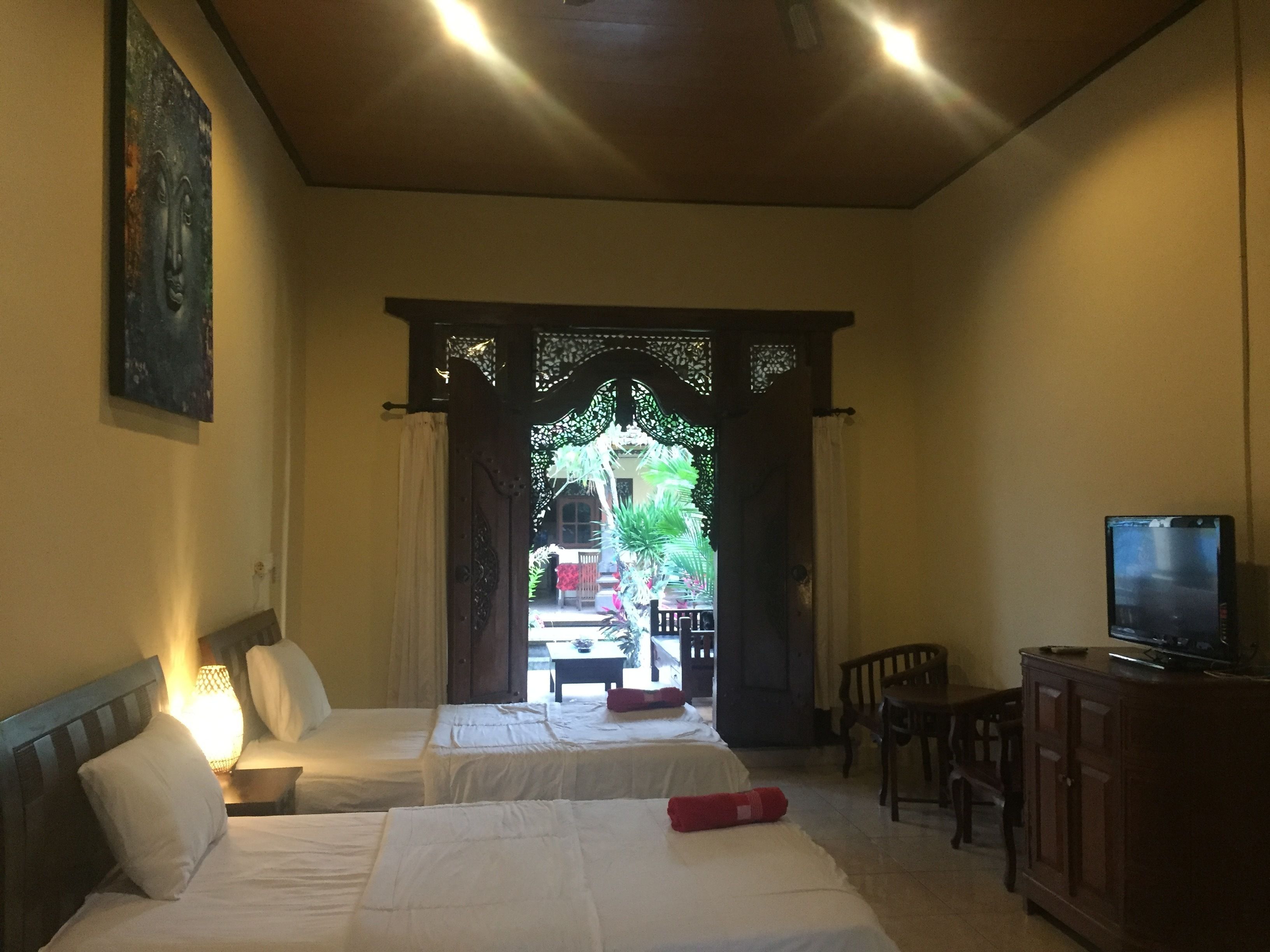 A hotel room with two beds, a TV, a desk, and a view of the outside through a decorative door.