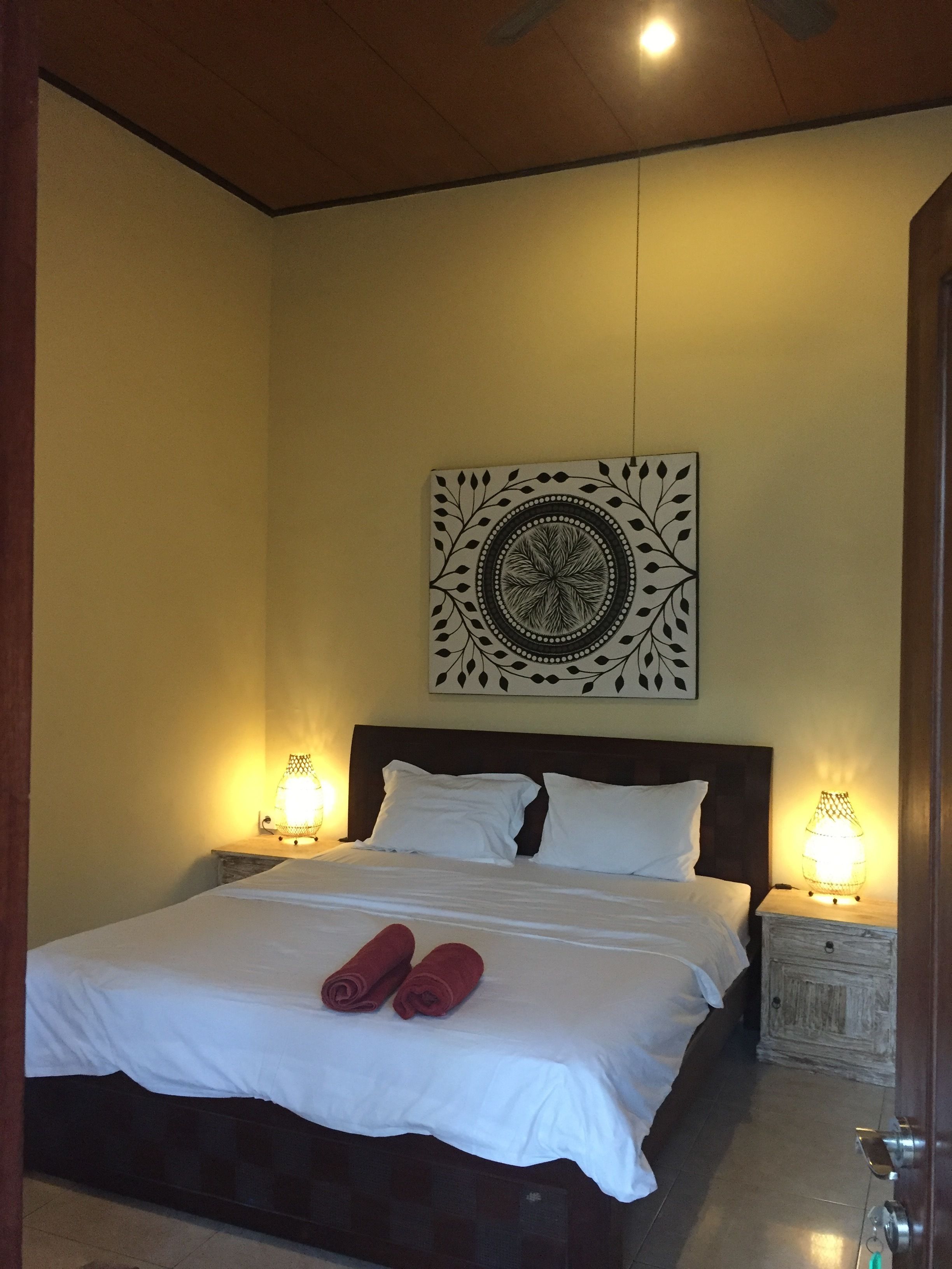 A neatly made bed with white linens and two red towels, a wall-mounted decorative piece, and two bedside lamps.