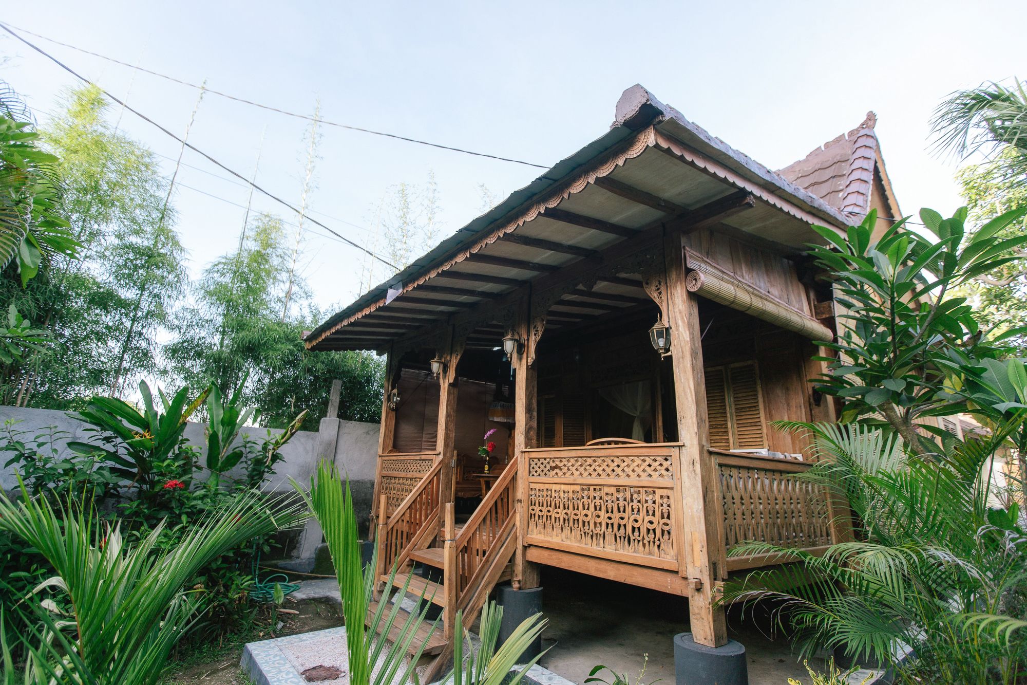 A traditional wooden house with a porch, surrounded by lush greenery.