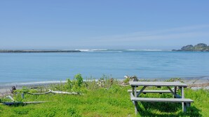 Ein Holztisch für ein Picknick am ruhigen Meer, mit grünen Wiesen und Felsen in der Ferne.