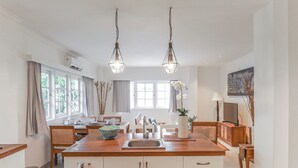 A modern kitchen with a central island, pendant lighting, and a dining area with a view of the outdoors. - Umalas Suite (Kerobokan)