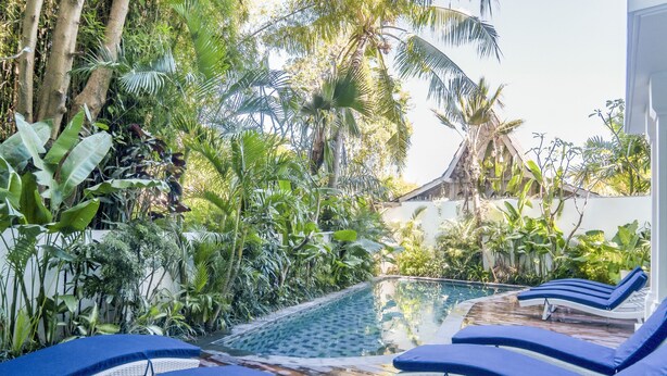 A poolside area with lounge chairs and tropical vegetation. - Umalas Suite (Kerobokan)