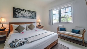 A neatly arranged hotel room with a large bed, a wooden bench, and a window with a view of greenery. - Umalas Suite (Kerobokan)