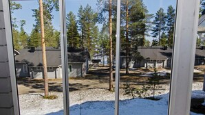 Vista a través de una ventana de una zona residencial con casas, árboles y suelo nevado.