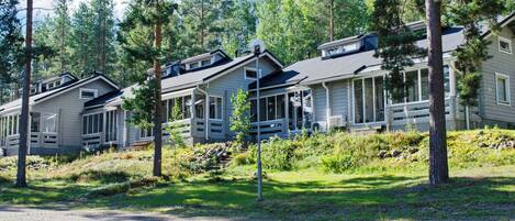 A row of cabins with attached porches, surrounded by trees and a gravel path.