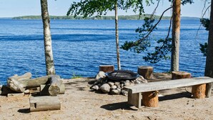 Un camping frente al lago con un brasero, bancos y vistas al agua.