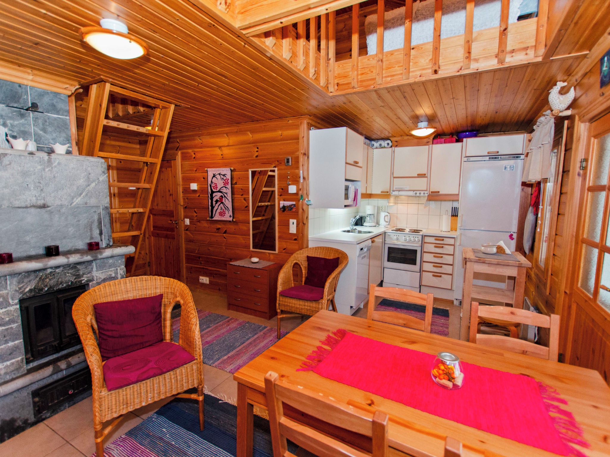 Ein gemütliches Blockhaus-Interieur mit Kamin, Holztisch, Korbstühle und einer Küchenzeile.