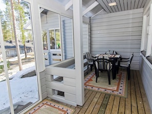 Een overdekt terras met een tafel, stoelen, een vloerkleed met patroon en uitzicht op de omgeving.