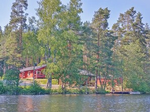 A lakeside cabin with a red exterior, surrounded by dense forest, and a dock extending into the water.