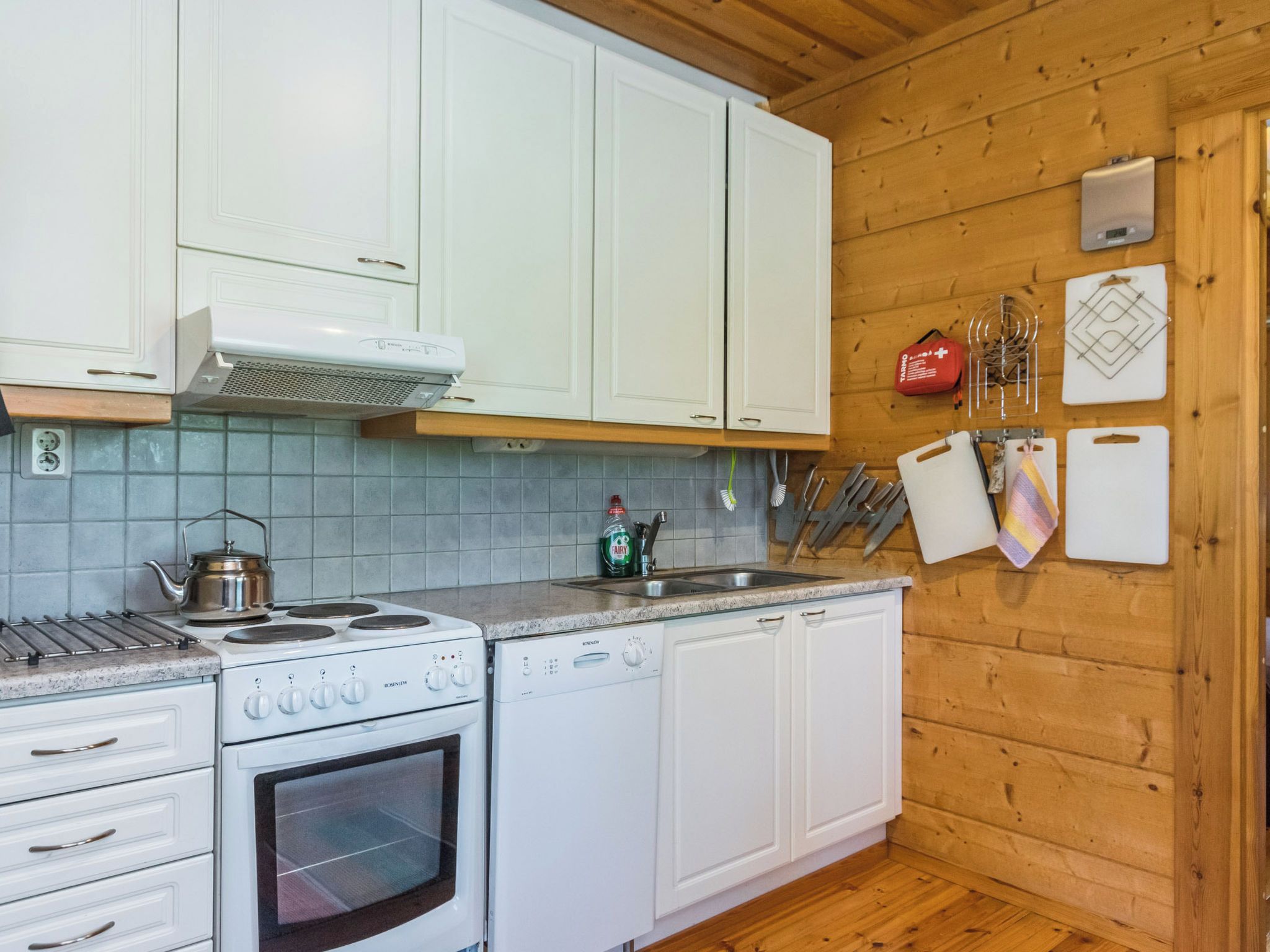 A kitchen with white cabinets, a stove, a dishwasher, and a wooden wall.