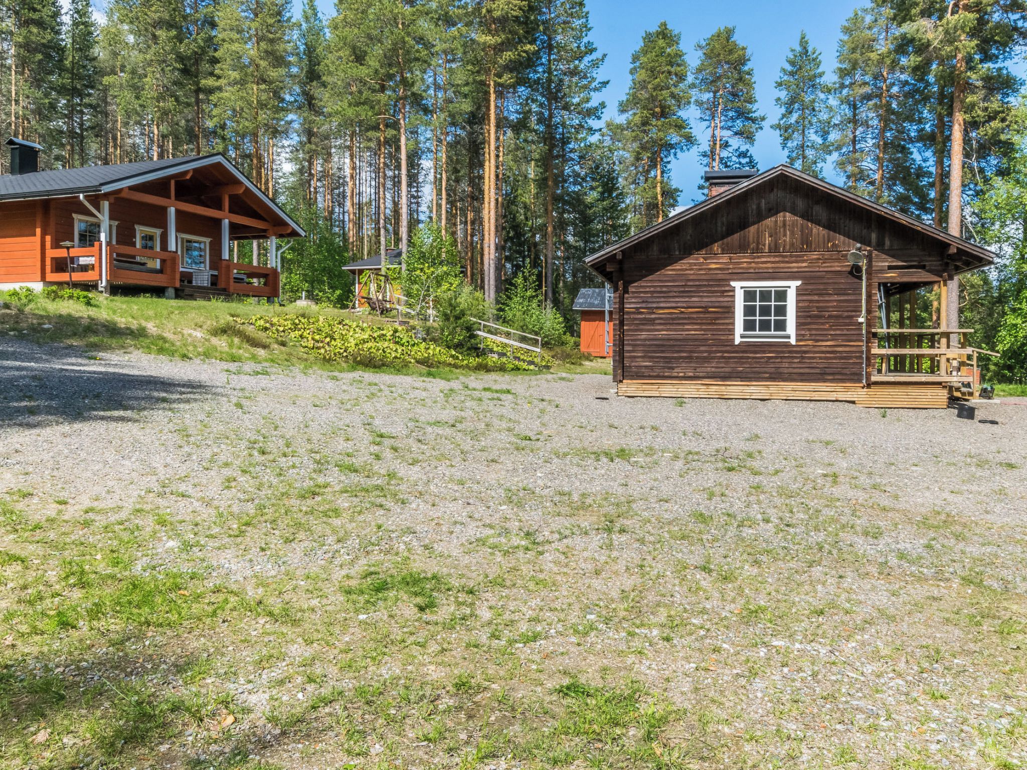 Een chalet met een houten gevel, een veranda en een oprit van grind.