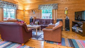 Un intérieur chaleureux de chalet en bois, avec des canapés en cuir, une table basse, un meuble pour la télévision et une cheminée.