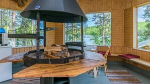 Un chalet confortable doté d’un poêle à bois central, de murs en bois et de grandes fenêtres donnant sur une zone boisée.