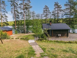 A cabin with a metal roof, a ladder, and a small shed in a wooded area with a lake.